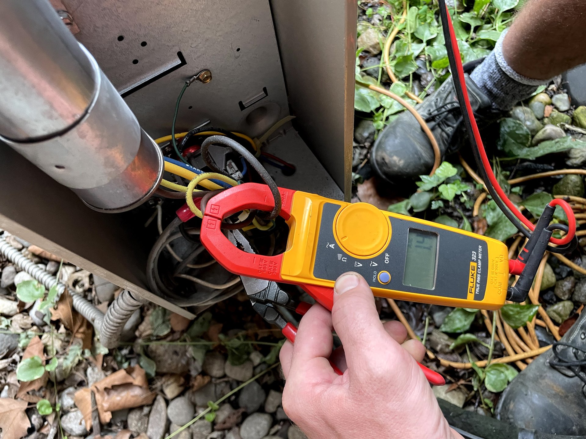 FastFix HVAC technician using Fluke clamp meter to diagnose outdoor AC condenser unit